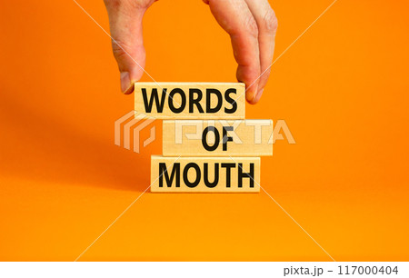 Words of mouth symbol. Concept words Words of mouth on wooden blocks on a beautiful orange table orange background. Businessman hand. Business, finacial and words of mouth concept. Copy space. 117000404