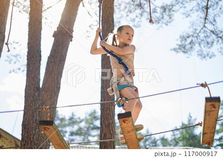 A brave strong girl in hiking gear walks the track on a suspension bridge at a height 117000917