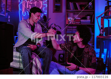 Two guys giving bro handshake after game challenge in retro dorm room 117003116