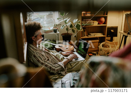 High angle shot of curly-haired student practicing coding while having online code course in messy dorm room 117003171