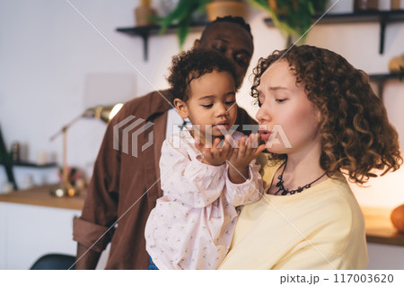 Cute child opening hands while carried by loving mother together with father in room 117003620