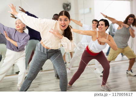 Smiling young woman rehearsing modern dance with group in dance school 117005617