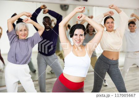 Cheerful young lady learning new modern dance in group dance lesson Cheerful young lady learning new modern dance in group dance lesson 117005667