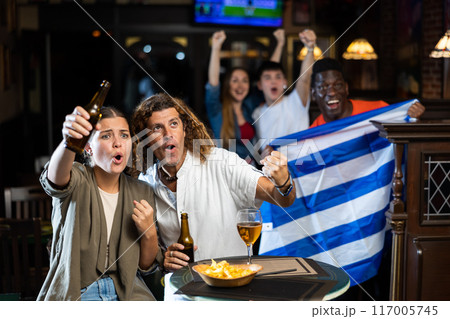 Excited couple rooting for Greek football team in sports bar 117005745