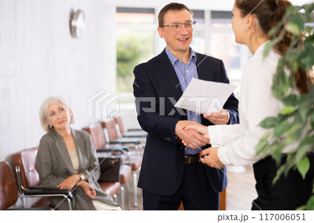 Smiling young girl makes deal, shaking hands with man colleague while standing in office. 117006051