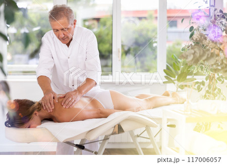 male masseur giving massage to female patient 117006057