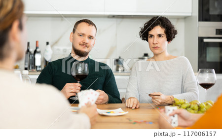 Friendly company of men and women sitting at kitchen table and enjoying the poker game. Friends play a card game at home. Evening entertainment concept 117006157