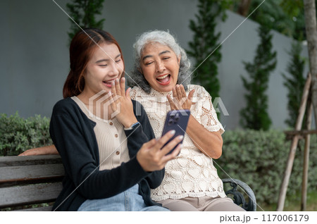 A happy retired Asian grandma is laughing and enjoying talking with her granddaughter in a garden. 117006179