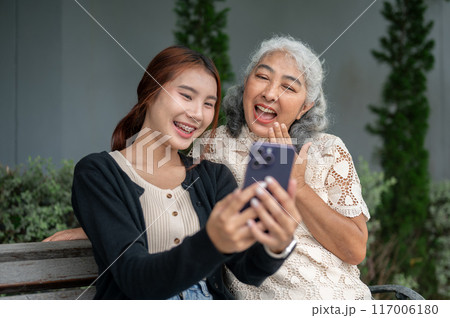 A happy retired Asian grandma is laughing and enjoying talking with her granddaughter in a garden. 117006180