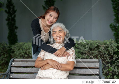A lovely Asian granddaughter is embracing her grandma with love while resting in a garden together. 117006182