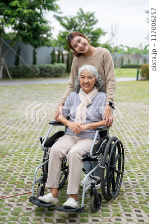 A charming Asian granddaughter and a happy grandmother in a wheelchair are in a park together. A charming Asian granddaughter and a happy grandmother in a wheelchair are in a park together. 117006257