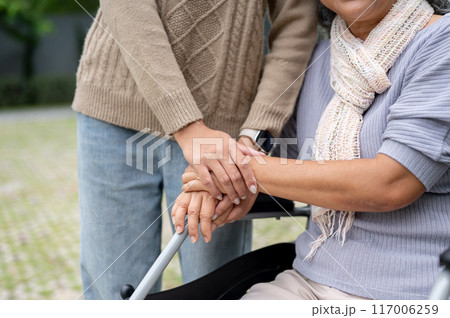 A close-up image of a daughter holding her mom's hand while she is in a wheelchair. 117006259