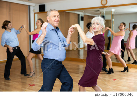 Cheerful elderly couple practicing ballroom dances in ballroom 117006346