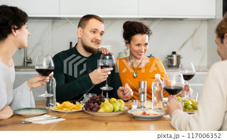 Group of joyful individuals are celebrating a holiday, enjoying drinks and conversation around table in their home Group of joyful individuals are celebrating a holiday, enjoying drinks and conversation around table in their home 117006352