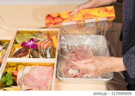 おせちのお肉をサランラップに包むシニア女性 117006800