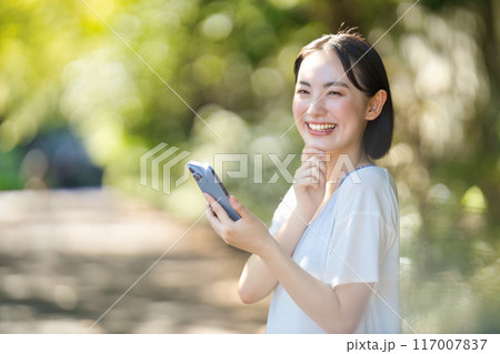 日差しの中でスマホを見る若い女性 117007837
