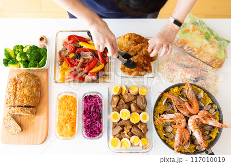 作り置き料理を盛り付けしているエプロン姿の女性 117010019