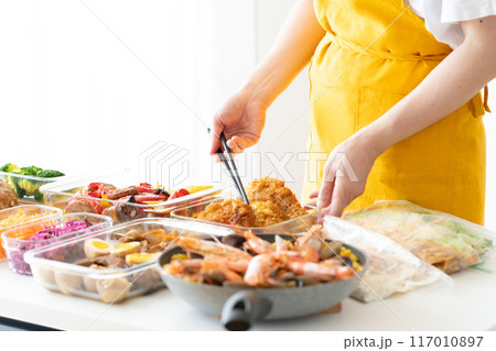 作り置き料理を盛り付けるエプロン姿の女性 117010897
