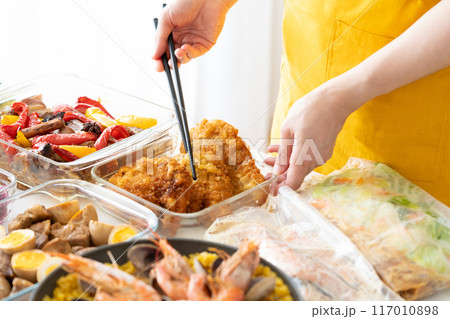 作り置き料理を盛り付けるエプロン姿の女性 117010898