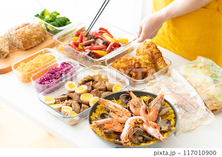 作り置き料理を盛り付けるエプロン姿の女性 作り置き料理を盛り付けるエプロン姿の女性 117010900