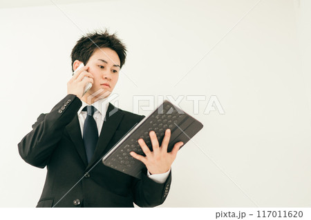 資料を見ながら電話をしているスーツ姿の20代男性 117011620
