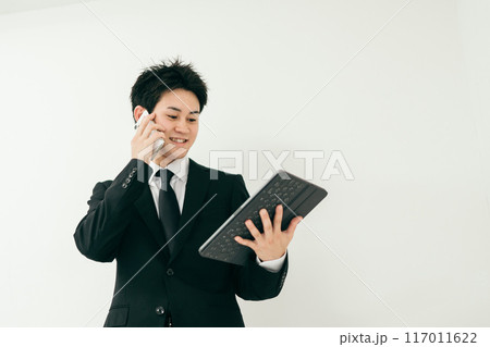 資料を見ながら電話をしているスーツ姿の20代男性 資料を見ながら電話をしているスーツ姿の20代男性 117011622