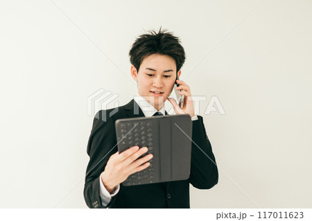 資料を見ながら電話をしているスーツ姿の20代男性 117011623