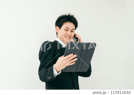 資料を見ながら電話をしているスーツ姿の20代男性 資料を見ながら電話をしているスーツ姿の20代男性 117011630