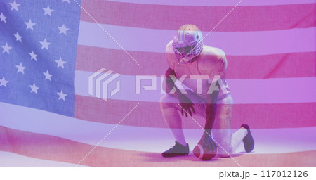 Image of african american american football player kneeling with ball and flag of usa 117012126