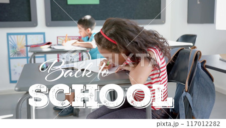 Back to school text over children studying in classroom, image 117012282