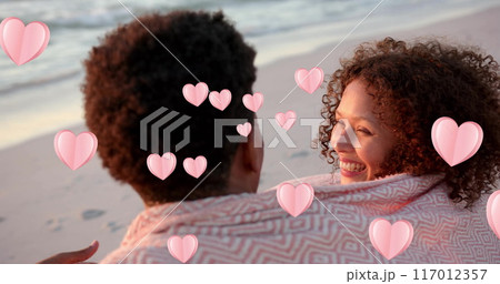 Image of hearts moving over diverse couple in love embracing on beach in summer 117012357