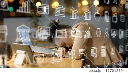Image of business icons over tired african american businesswoman waking up at office desk 117012394