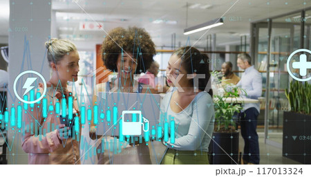 Image of graph and energy icons over diverse female colleagues using laptop at casual office 117013324