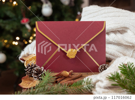 Red envelope near pine cones, spices, white knitted sweater and fir twigs. Christmas mockup Red envelope near pine cones, spices, white knitted sweater and fir twigs. Christmas mockup 117016062