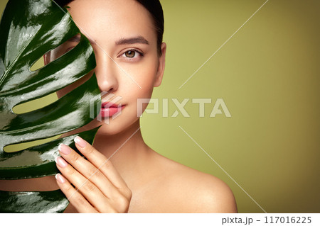 Close up woman face with green exotic leaf Close up woman face with green exotic leaf 117016225