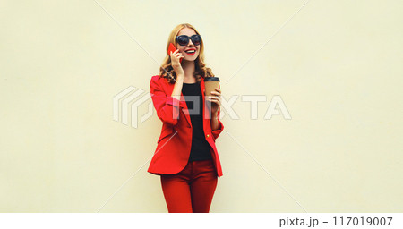 Beautiful young woman calling on smartphone in red business suit on white background 117019007