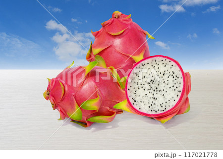 Dragon fruit, red-green peel fruit isolated on a white wooden table with a bright sky in the background Dragon fruit, red-green peel fruit isolated on a white wooden table with a bright sky in the background 117021778