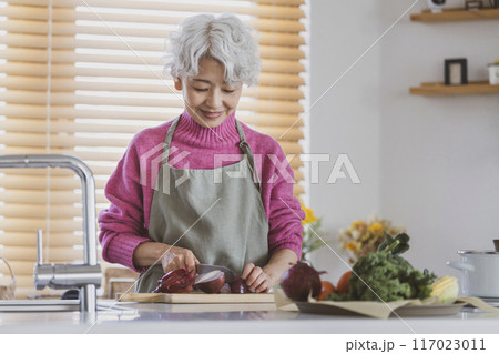 キッチンで野菜を切るシニア女性 117023011