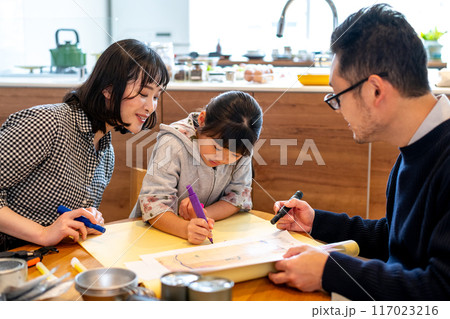 娘が避難する場所を大きな紙に記入する様子を覗き込みながら笑顔で見守るお母さん 娘が避難する場所を大きな紙に記入する様子を覗き込みながら笑顔で見守るお母さん 117023216