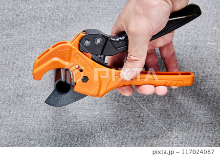 Scissors cutter for cutting pipes with ratchet mechanism, in man hand on gray background. Scissors cutter for cutting pipes with ratchet mechanism, in man hand on gray background. 117024087