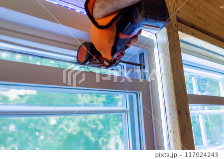 In new house, construction worker installs plastic windows using screwdriver 117024243