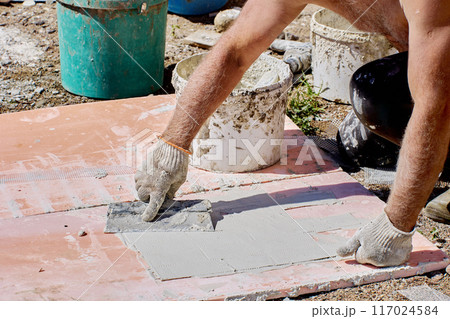 Homeowner DIYs facade trim using steel trowel to apply adhesive to panel of false brick. 117024584