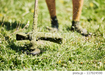 Close up of weed trimmer drum with protective guard and string while cutting grass. 117024590