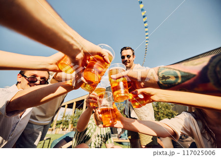 Cheers to summer. Friends raise their glasses in a joyful toast at a sunny picnic. Positive vibes of outdoor catering Cheers to summer. Friends raise their glasses in a joyful toast at a sunny picnic. Positive vibes of outdoor catering 117025006