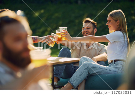 Positive young men and women,friends gathering outdoors in public place, enjoying company, conversation and beer 117025031