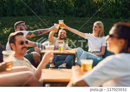 Positive young men and women,friends gathering outdoors in public place, enjoying company, conversation and beer 117025032