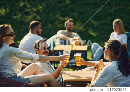 Cheers. Young smiling men and women,friends celebration, having party outdoors on warm summer day, cheerfully talking and drinking beer 117025035