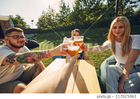 Happy young smiling people sitting outdoors in cafe, restaurant, enjoying refreshing beer, clinking glasses. Celebration, party Happy young smiling people sitting outdoors in cafe, restaurant, enjoying refreshing beer, clinking glasses. Celebration, party 117025061