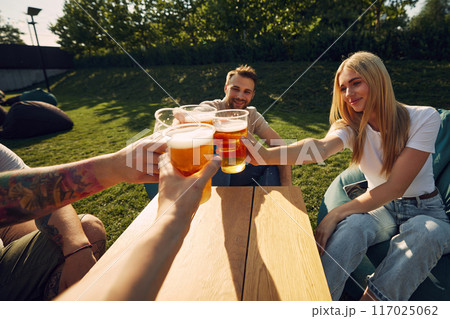 Happy young smiling people sitting outdoors in cafe, restaurant, enjoying refreshing beer, clinking glasses. Happy young smiling people sitting outdoors in cafe, restaurant, enjoying refreshing beer, clinking glasses. 117025062
