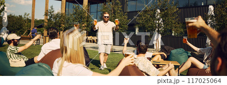 Lively event. Happy young people, friends gathering in outdoor cafe space, having outdoor picnic with refreshing beer and cheerful talks 117025064